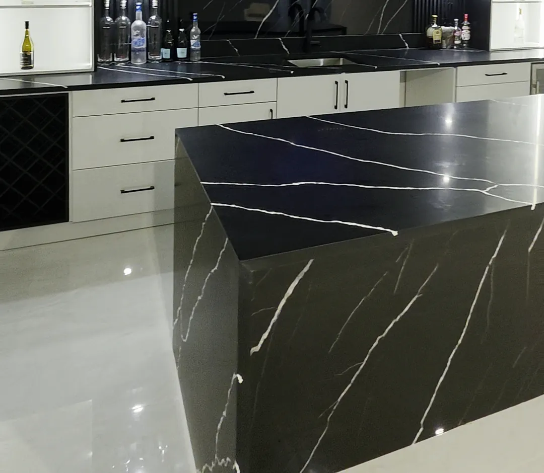 Long side of a black waterfall island with white veining in front of a white-cabinet back bar