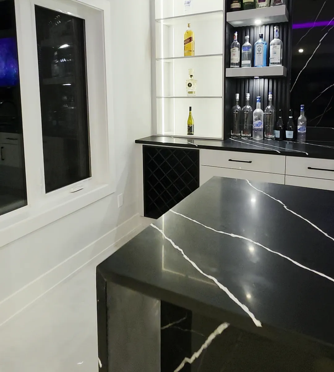 Waterfall end of a black stone island next to lit bar shelving