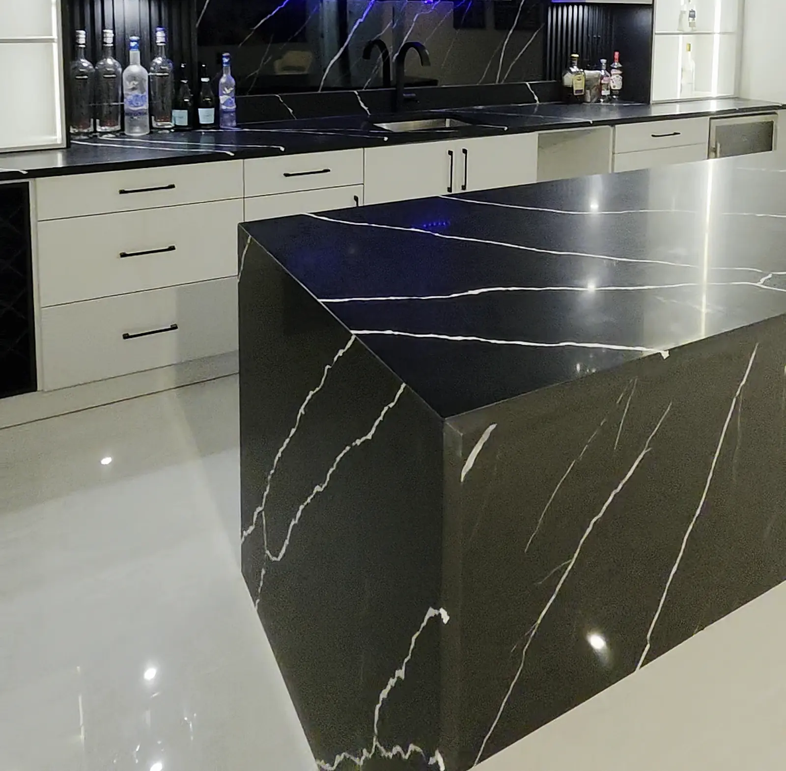 Black stone waterfall island with bold white veining, with the back bar counter, sink and backsplash behind it